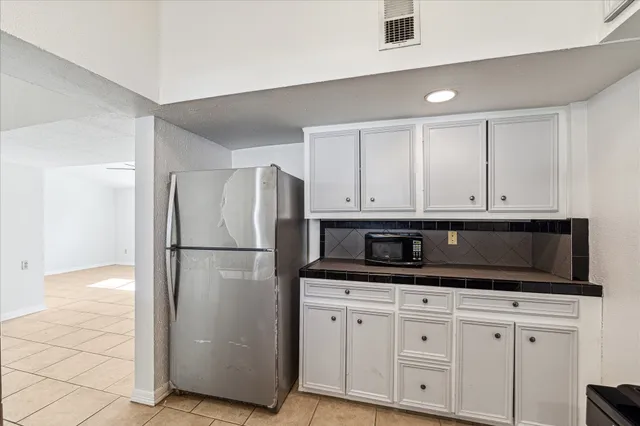a kitchen with granite countertop a refrigerator a sink and white cabinets