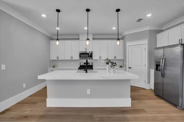 a kitchen that has a sink a microwave oven a stove and white cabinets with wooden floor