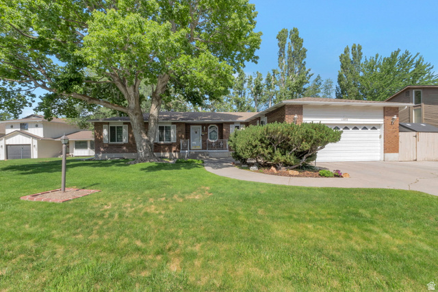 Brick exterior featuring a two-car garage, mature landscaping, and a concrete driveway