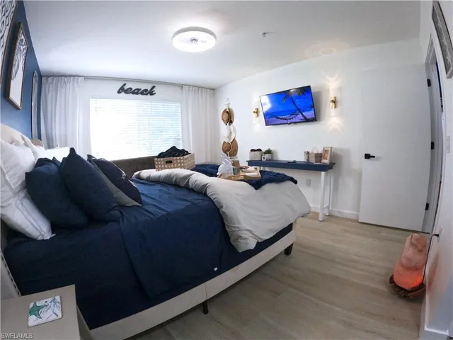 a bedroom with bed and a lamp on dresser with wooden floor