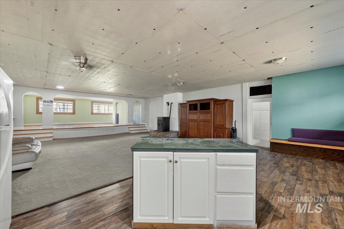 2160 South Five Mile Road Boise, ID 83709 - Photo 30 of 41 Spacious open room featuring wood-finish flooring, a white cabinet island with a dark countertop, and a raised platform with arched openings