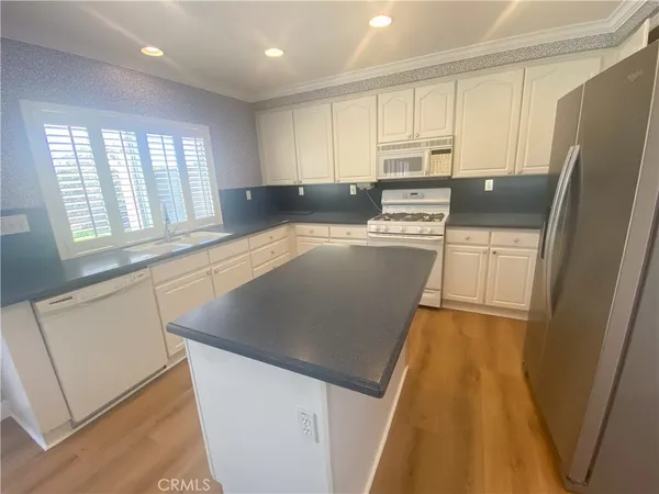 a kitchen with stainless steel appliances granite countertop a refrigerator a sink dishwasher a stove and white countertops with wooden floor