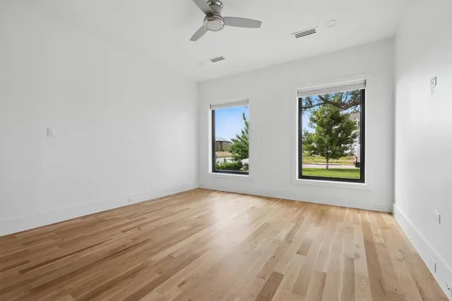an empty room with wooden floor windows and ceiling fan