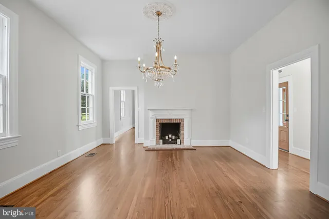 a view of an empty room with wooden floor fireplace and a window