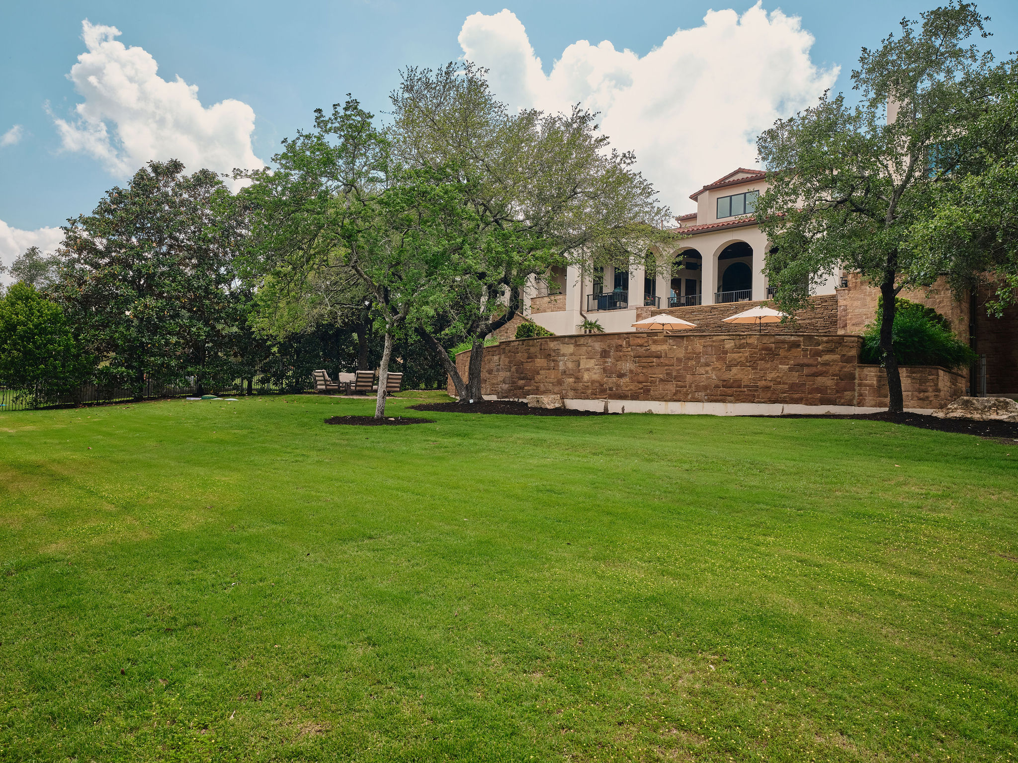 433 Brandon Way Austin, TX 78733 - Photo 39 of 40 Manicured green lawn unfolds before a grand residence with arched loggias and a stone retaining wall.