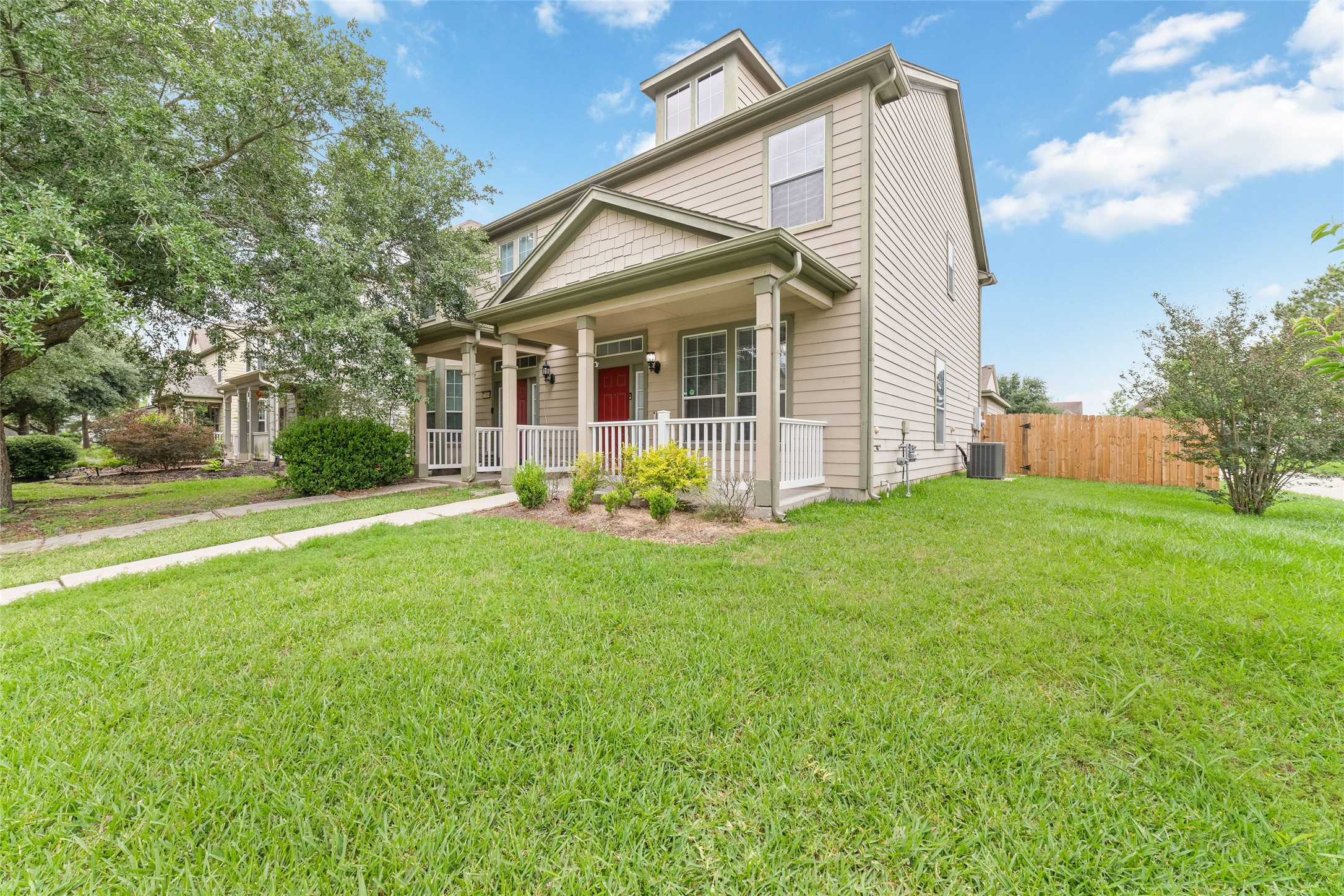 23602 Youpon Lake Lane Spring, TX 77373 - Photo 2 of 21 Corner lot exterior showcasing lush green space, covered front porch seating, and charming curb appeal surrounded by mature greenery.