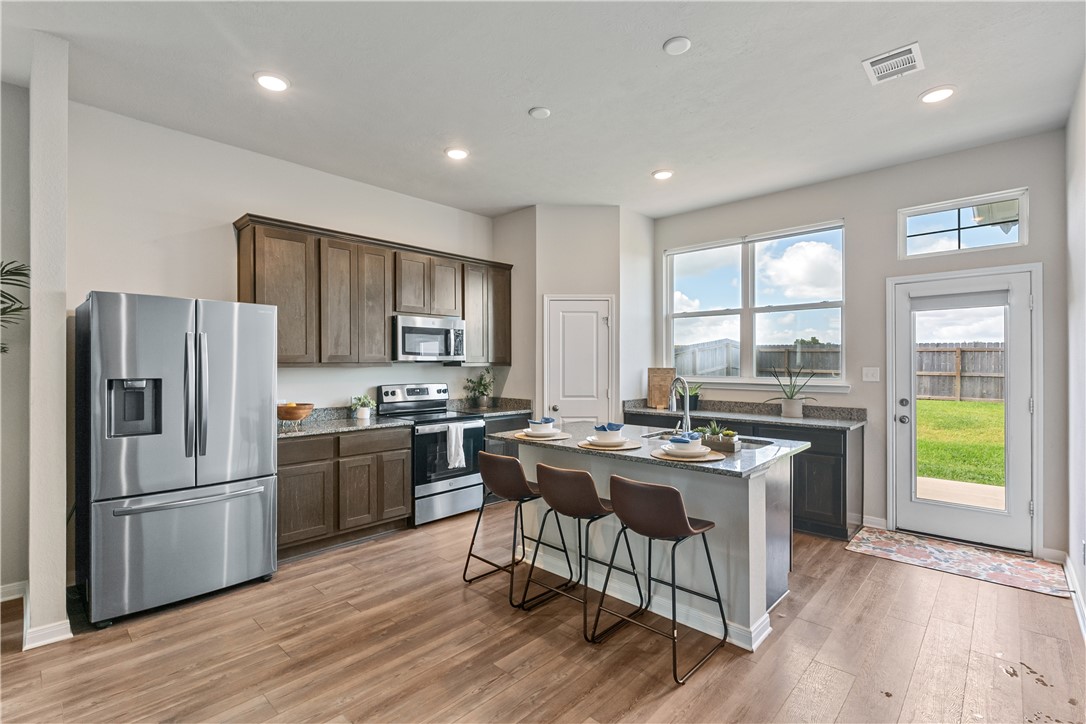 4746 Holm Oak Road College Station, TX 77845 - Photo 9 of 25 a kitchen with stainless steel appliances granite countertop a stove a refrigerator a sink a stove and island with wooden floor