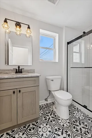 a bathroom with a granite countertop toilet a sink a mirror and a shower
