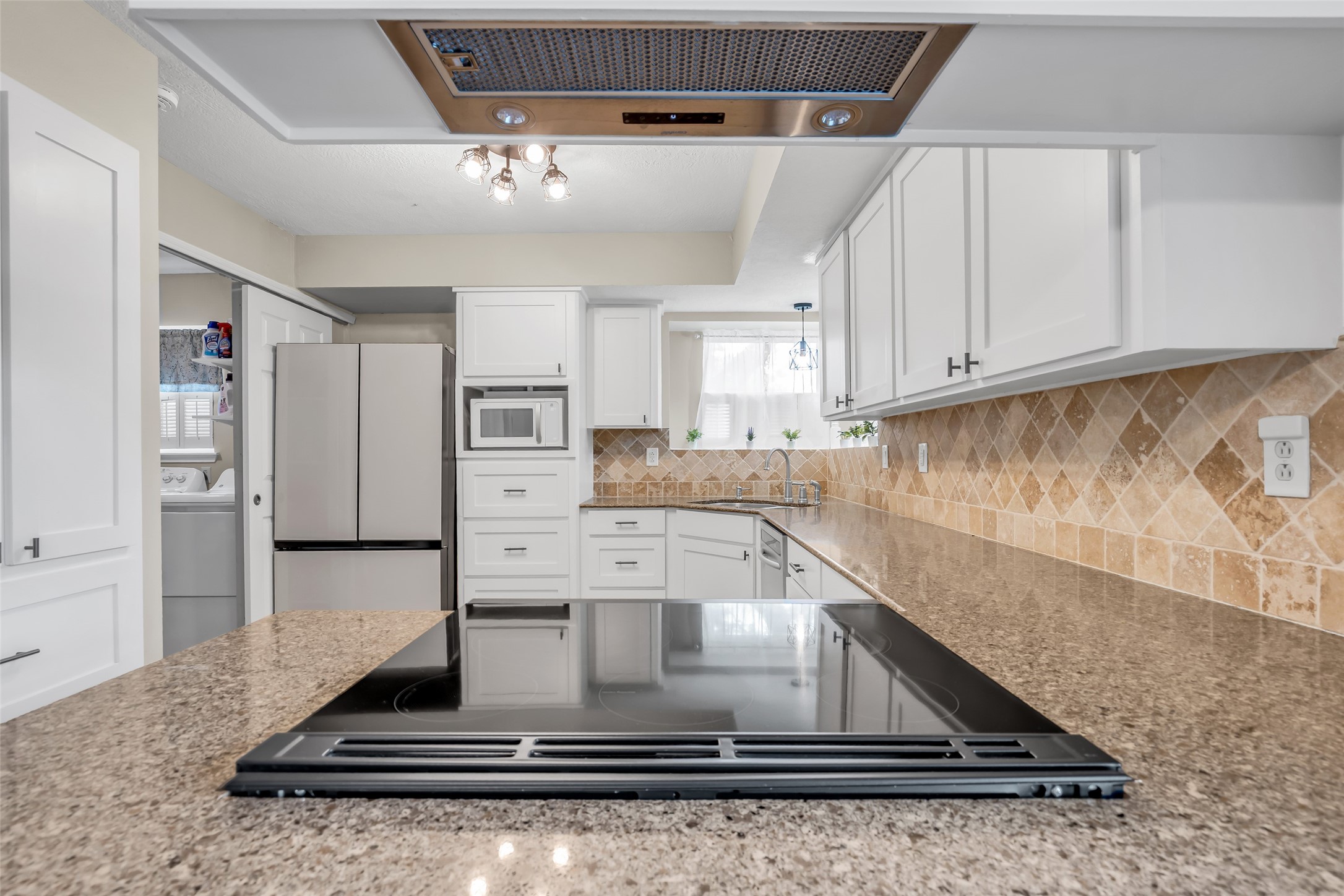22502 Fields Lane Spring, TX 77389 - Photo 13 of 39 This kitchen features modern white cabinetry, a sleek electric cooktop, and a spacious granite countertop. It includes stainless steel appliances and a tiled backsplash, creating a clean and inviting cooking space.