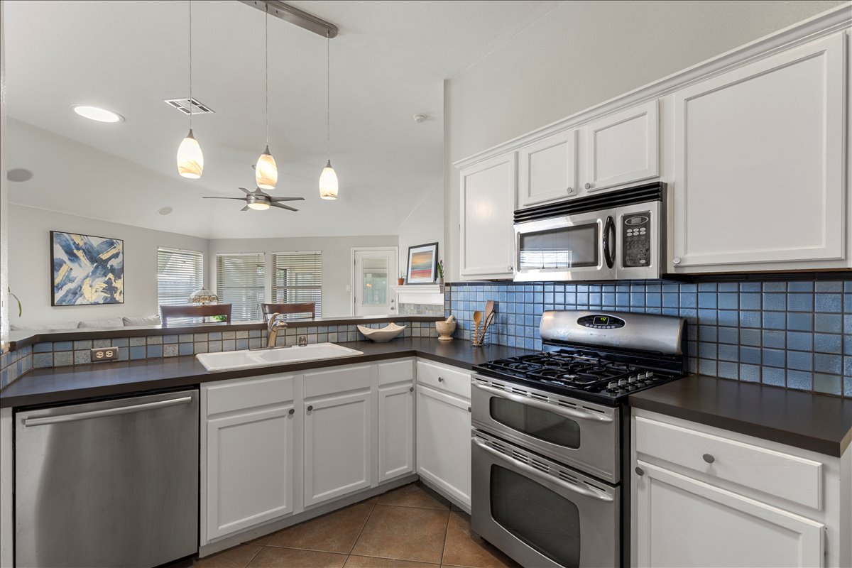 9012 Meacham Way Austin, TX 78749 - Photo 8 of 34 Kitchen featuring white cabinetry, dark countertops, stainless steel appliances, a blue tile backsplash, and a double basin sink
