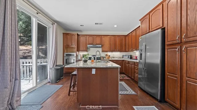 a kitchen with stainless steel appliances granite countertop wooden cabinets a refrigerator a stove a sink and dishwasher with wooden floor