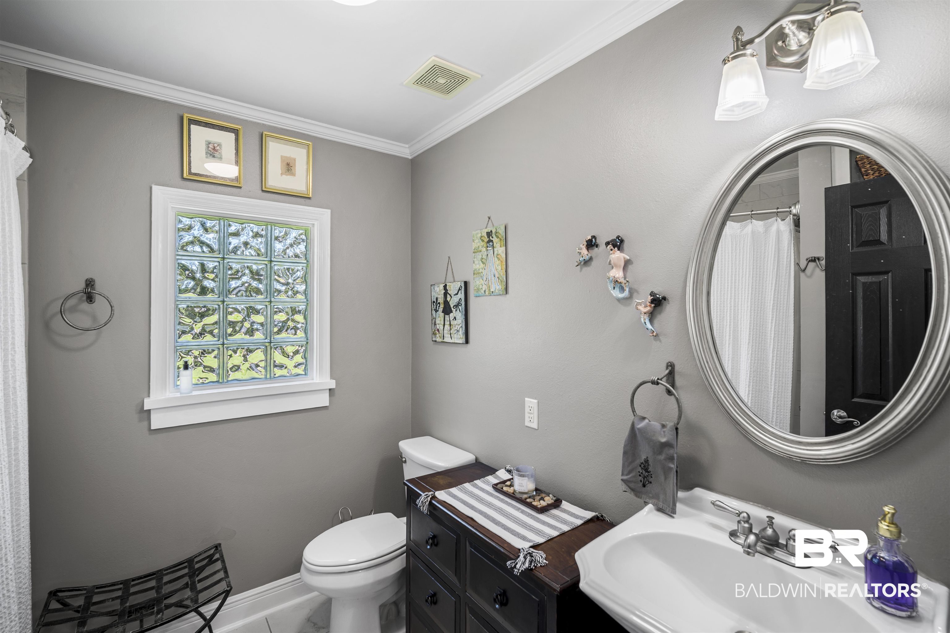 1615 5th Street Daphne, AL 36526 - Photo 21 of 28 Bathroom featuring a glass block window, oval mirror, wall-mounted vanity light, white sink, and dark wood-finish vanity