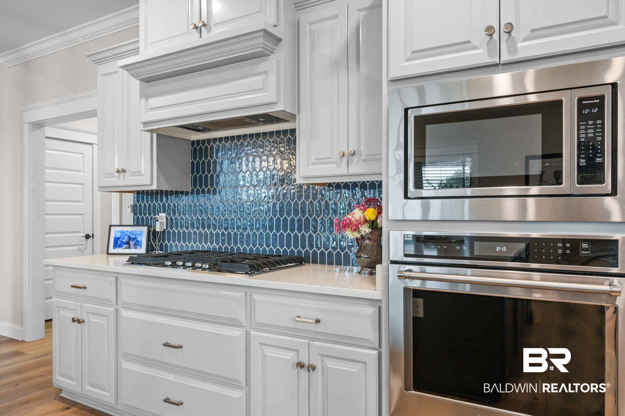 409 Fortune Drive Fairhope, AL 36532 - Photo 12 of 42 Kitchen featuring white cabinetry, a blue picket tile backsplash, a gas cooktop, light-toned countertops, and stainless steel appliances including a built-in microwave and oven