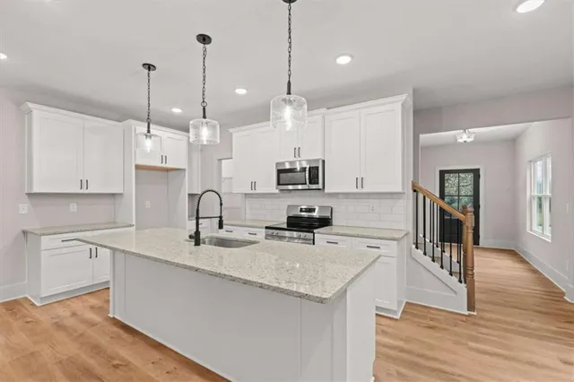 a kitchen with stainless steel appliances granite countertop a sink a stove a refrigerator and white cabinets with wooden floor