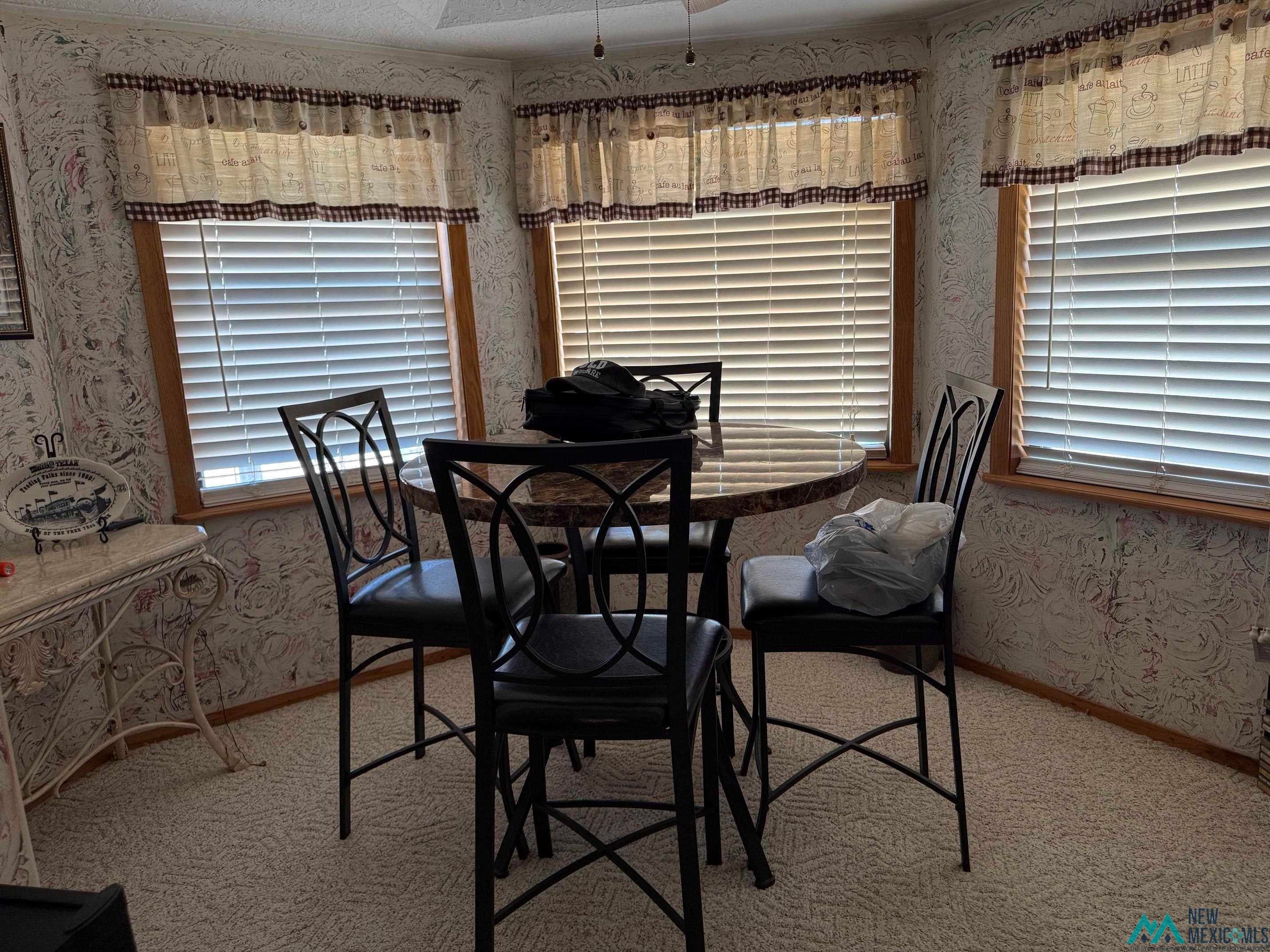 4010 540th Loop Logan, NM 88426 - Photo 8 of 38 Breakfast nook featuring multiple windows with horizontal blinds, patterned wallpaper, and light-toned carpet flooring