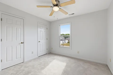 an empty room with chandelier fan and windows