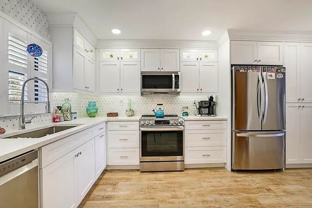 a white kitchen with stainless steel appliances granite countertop a refrigerator and a stove top oven