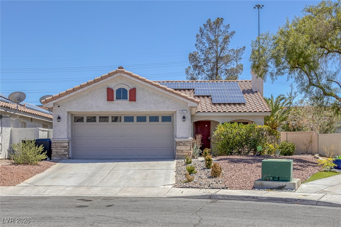 Mediterranean / spanish-style house with stone siding, a tiled roof, roof mounted solar panels, and concrete driveway
