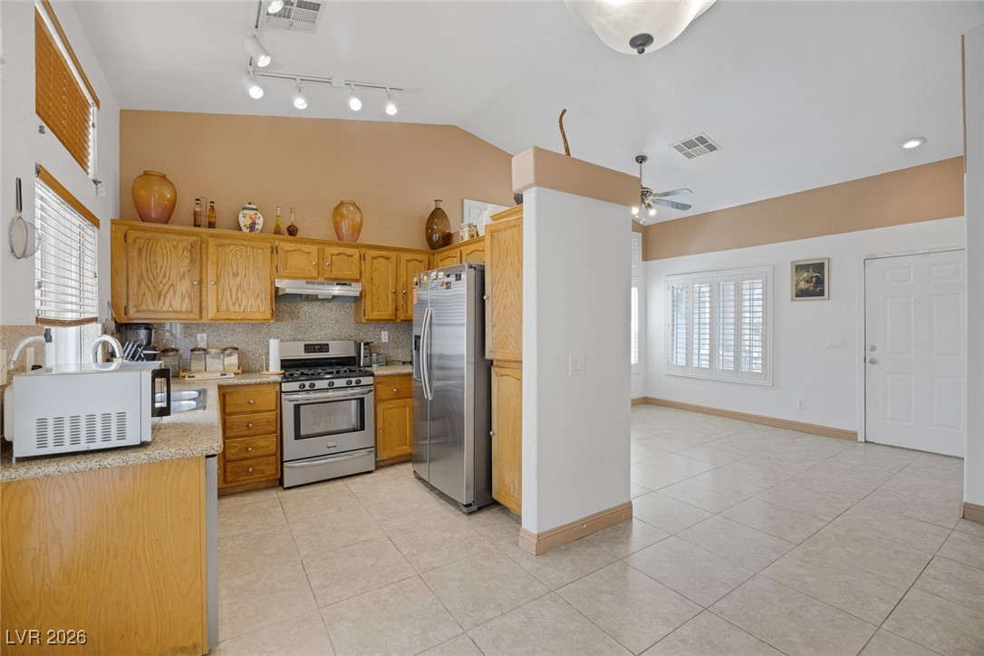 2427 Worchester Road Henderson, NV 89074 - Photo 11 of 35 Kitchen featuring stainless steel appliances, light tile patterned floors, decorative backsplash, under cabinet range hood, and lofted ceiling