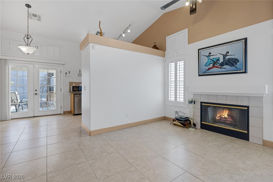 2427 Worchester Road Henderson, NV 89074 - Photo 8 of 35 Unfurnished living room featuring a tiled fireplace, light tile patterned floors, french doors, high vaulted ceiling, and rail lighting