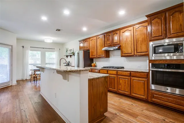 a kitchen with stainless steel appliances granite countertop wooden cabinets a sink a stove a dining table and chairs