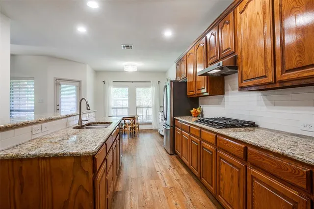 a kitchen with stainless steel appliances granite countertop a stove a sink dishwasher and a refrigerator with wooden floor