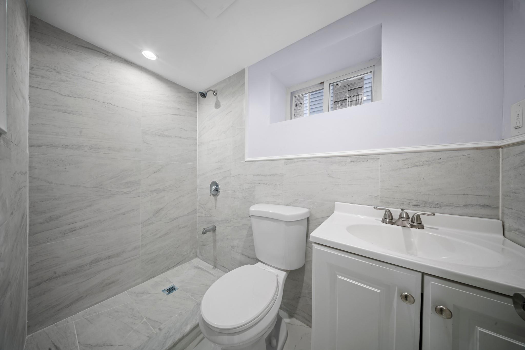 110-28 213th Street Queens, NY 11429 - Photo 16 of 22 Full bath with tiled shower, toilet, vanity, marble look tiles, and tile walls