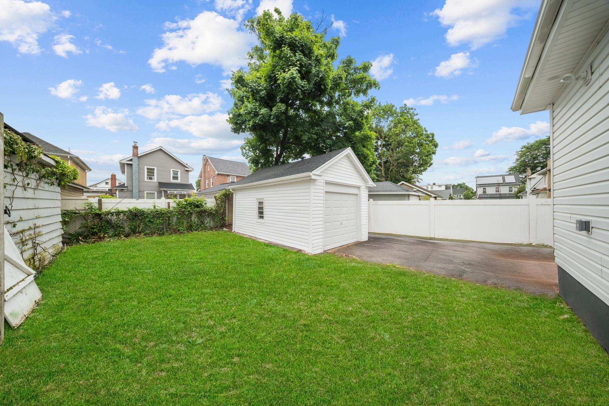 110-28 213th Street Queens, NY 11429 - Photo 18 of 22 View of yard with a garage, driveway, an outdoor structure, a patio, and a residential view