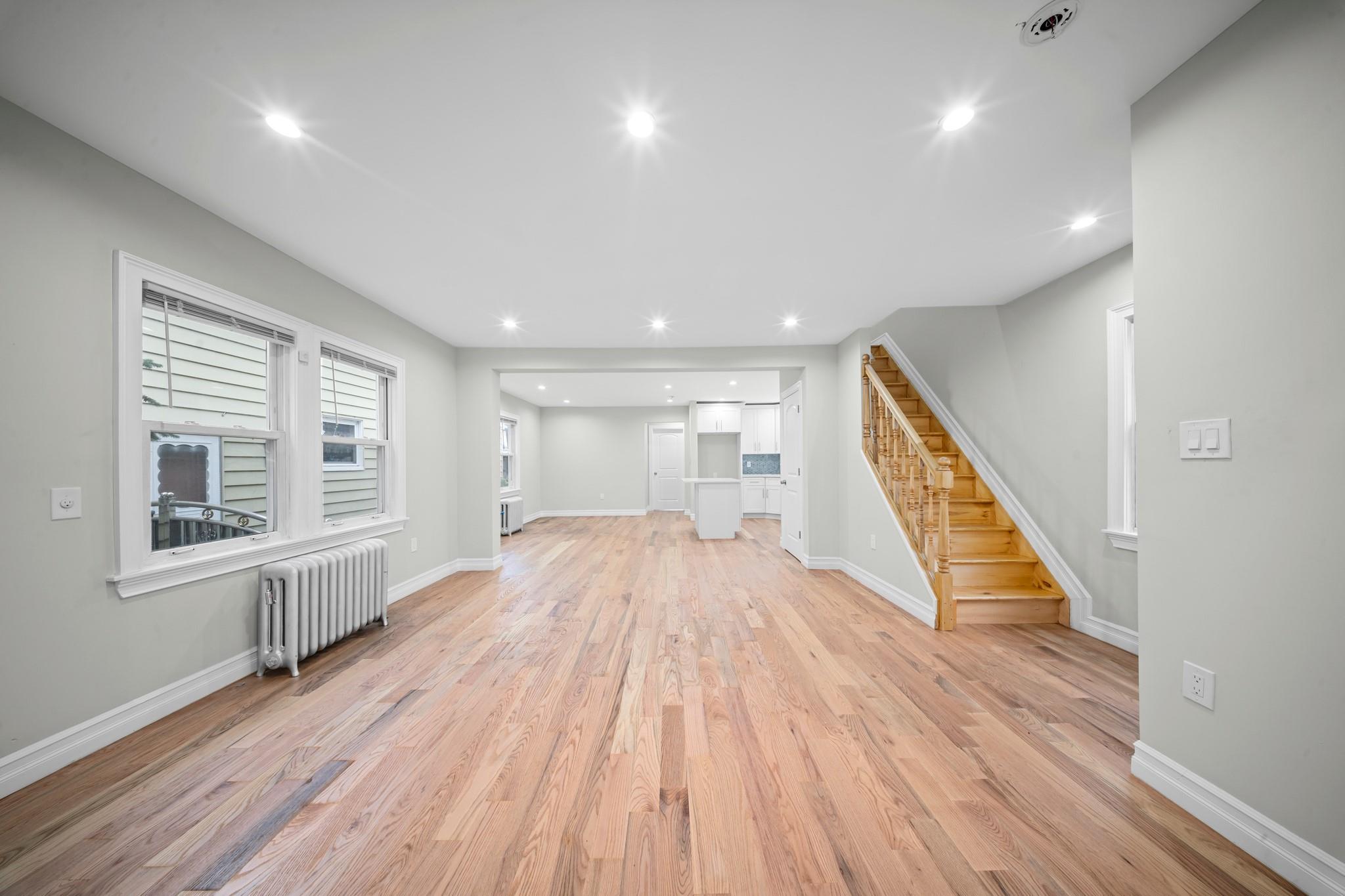 110-28 213th Street Queens, NY 11429 - Photo 6 of 22 Unfurnished living room with radiator heating unit, stairway, baseboards, light wood-style floors, and recessed lighting