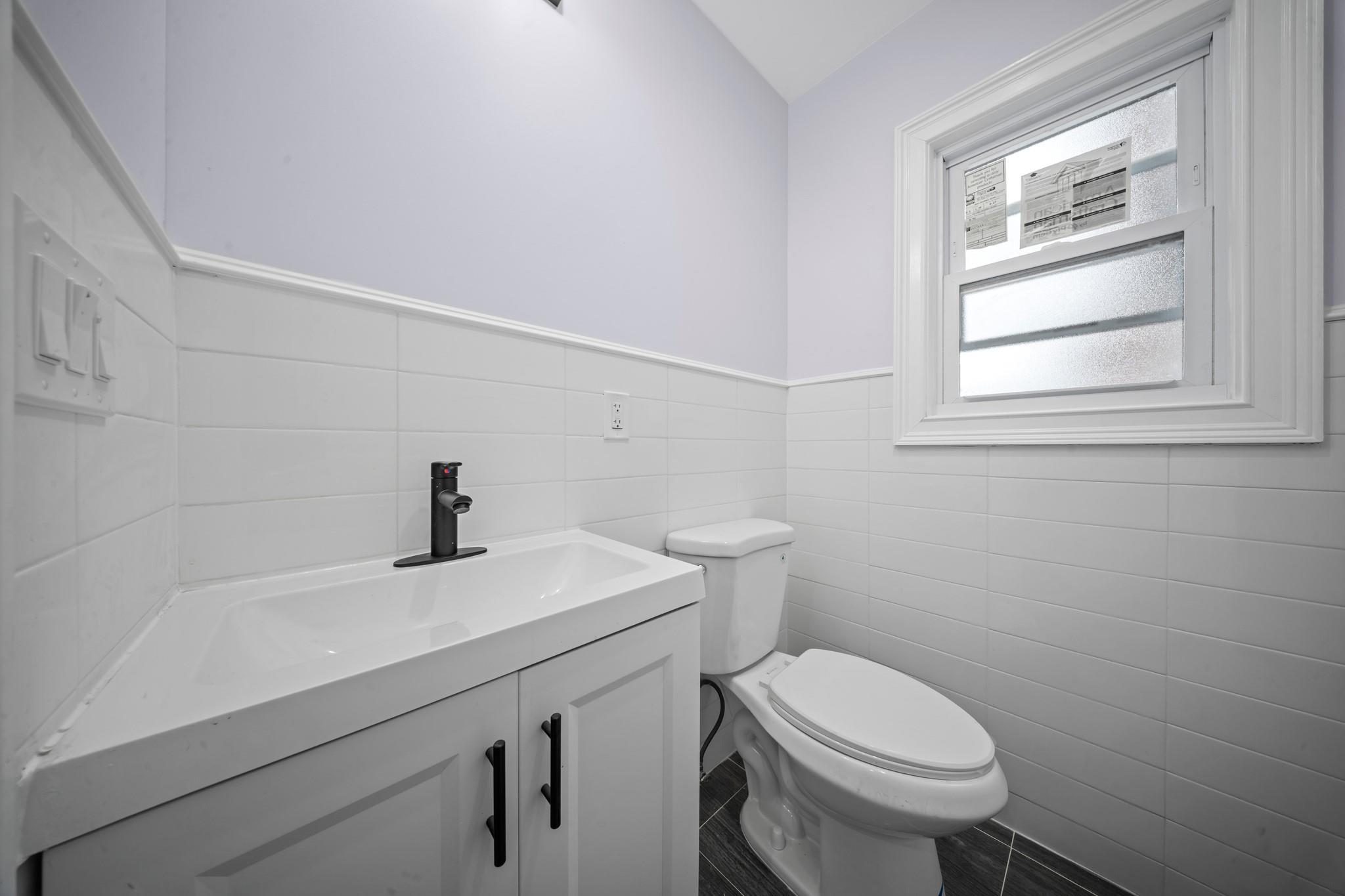 110-28 213th Street Queens, NY 11429 - Photo 7 of 22 Half bathroom featuring tile walls, toilet, vanity, and a wainscoted wall