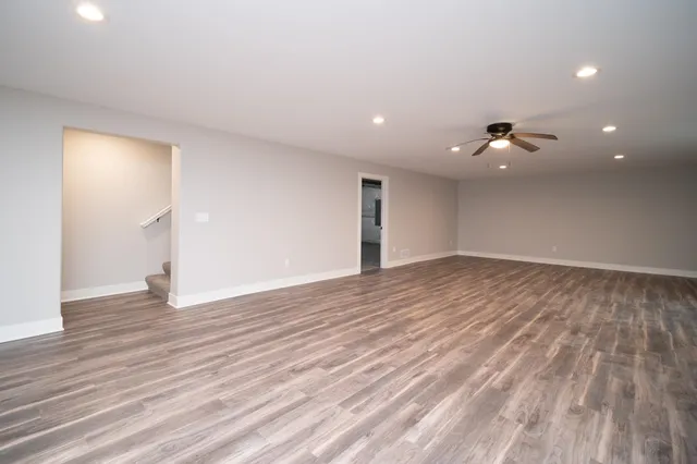 a view of an empty room with wooden floor and a ceiling fan