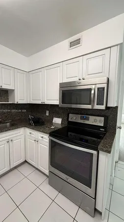 a kitchen with stainless steel appliances granite countertop white cabinets a stove a microwave and a sink