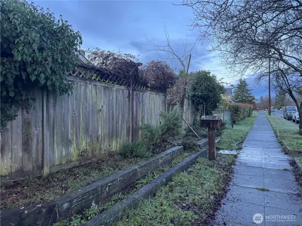 a view of a pathway of a park with plants and a bench with wooden fence