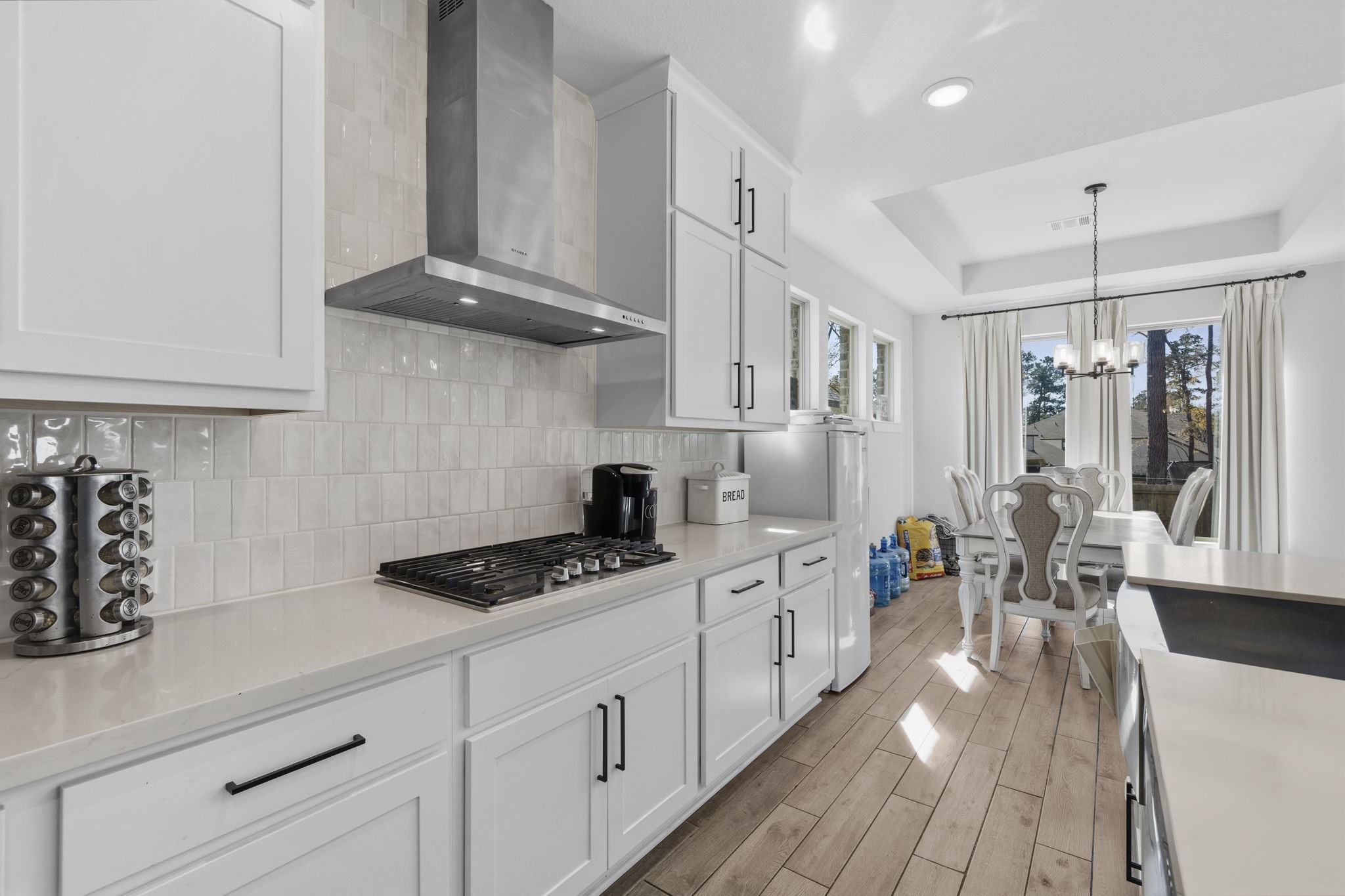 511 Carina Gaze Drive Conroe, TX 77318 - Photo 12 of 45 This bright kitchen and dining area features modern white cabinetry, a sleek gas cooktop, and stylish tile backsplash.