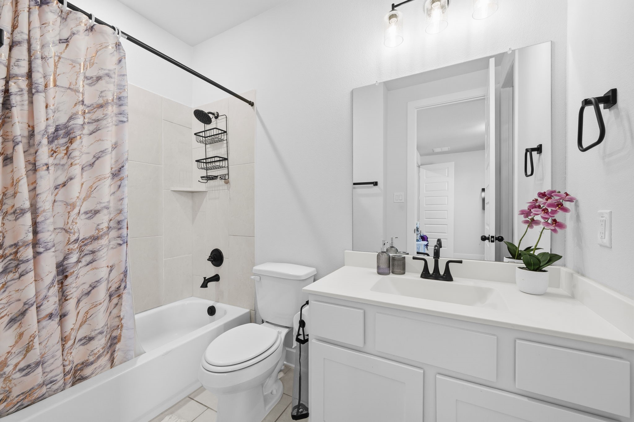511 Carina Gaze Drive Conroe, TX 77318 - Photo 21 of 45 This bathroom features a modern design with a white vanity, black fixtures, and a decorative shower curtain. It includes a bathtub, large mirror, and bright lighting, creating a fresh and inviting space.