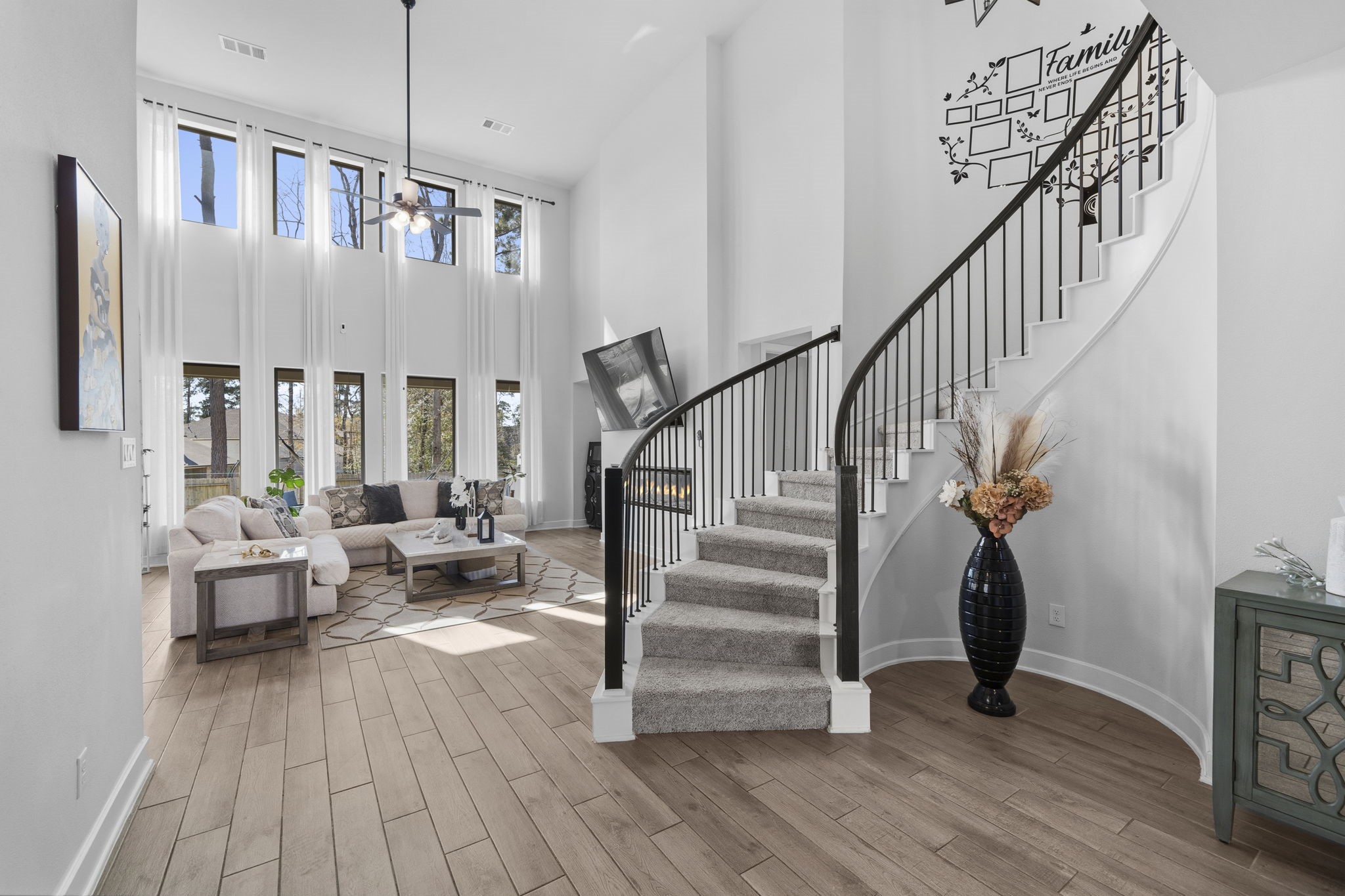 511 Carina Gaze Drive Conroe, TX 77318 - Photo 3 of 45 This stunning living room features a high ceiling with large windows that flood the space with natural light. A beautiful, curved staircase with Westin's rotunda adds elegance, while the open layout and modern decor create a welcoming atmosphere.