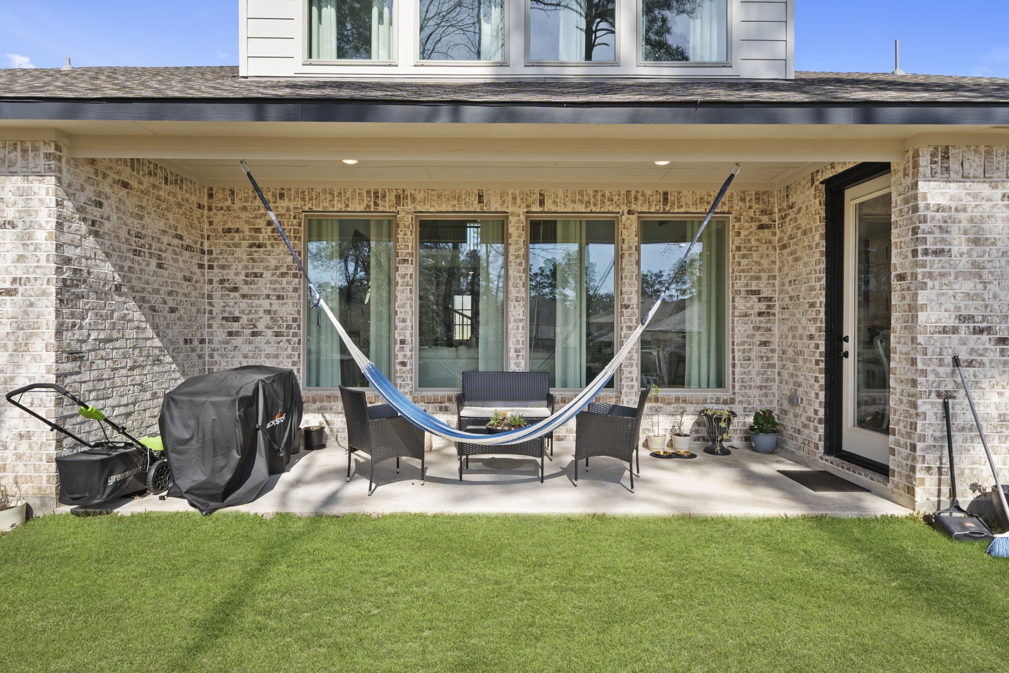 511 Carina Gaze Drive Conroe, TX 77318 - Photo 35 of 45 This inviting backyard patio features a cozy hammock, outdoor seating, and a barbecue area, all set against a beautiful brick exterior and lush green lawn. Perfect for relaxation and entertaining.