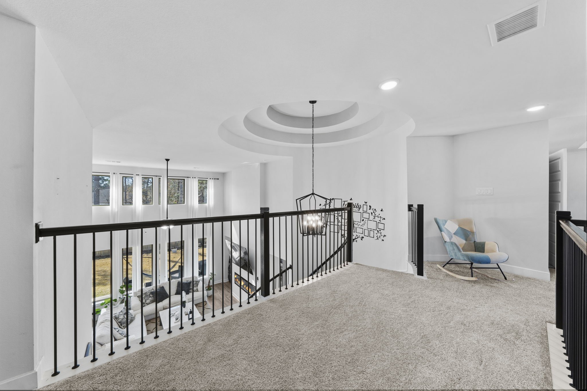 511 Carina Gaze Drive Conroe, TX 77318 - Photo 6 of 45 This photo showcases an open loft area with plush carpeting, a modern black railing, and a unique ceiling rotunda design. A cozy reading nook features a colorful chair, and large windows provide ample natural light, overlooking the spacious living area below.