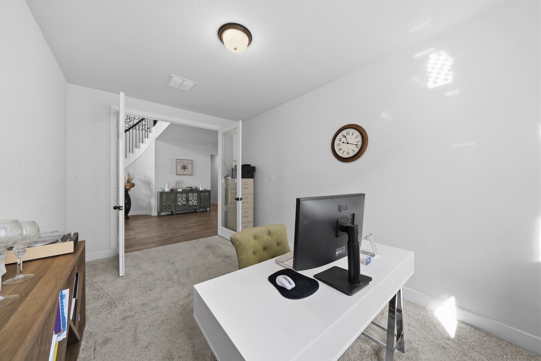 511 Carina Gaze Drive Conroe, TX 77318 - Photo 7 of 45 Bright home office with carpeted flooring, featuring a modern desk setup. French doors open to a hallway with wood like tile floors and a staircase, offering a glimpse of stylish decor.