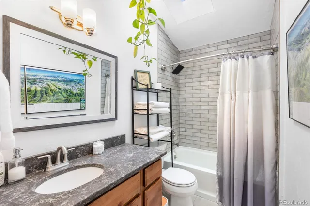 a bathroom with a granite countertop sink a toilet a mirror a vanity and shower