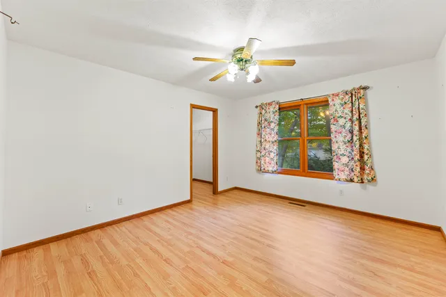 an empty room with wooden floor chandelier fan and windows