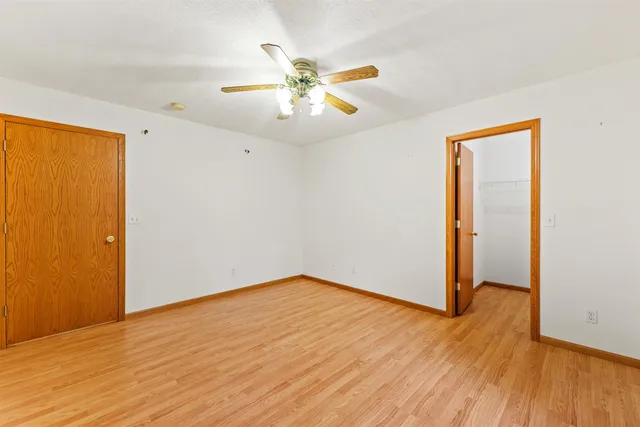 an empty room with wooden floor fan and windows