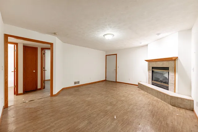 an empty room with wooden floor fireplace and windows