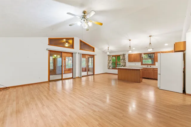 a view of an empty room with wooden floor and a kitchen