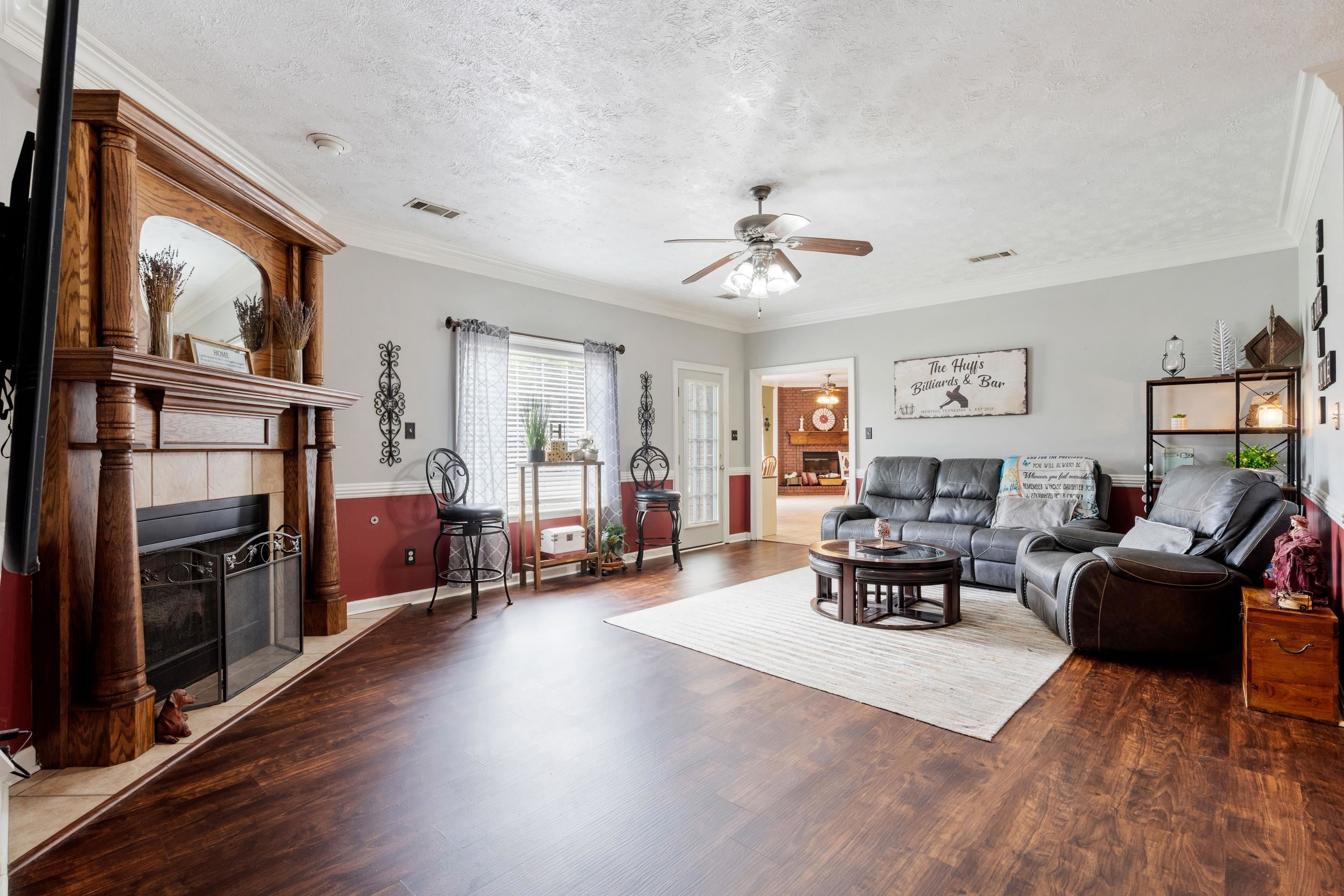 7757 Brunswick Road Millington, TN 38053 - Photo 6 of 40 Spacious living area featuring wood-finish flooring, a traditional wood mantel fireplace with tile surround, a ceiling fan, crown molding, and a large window with blinds