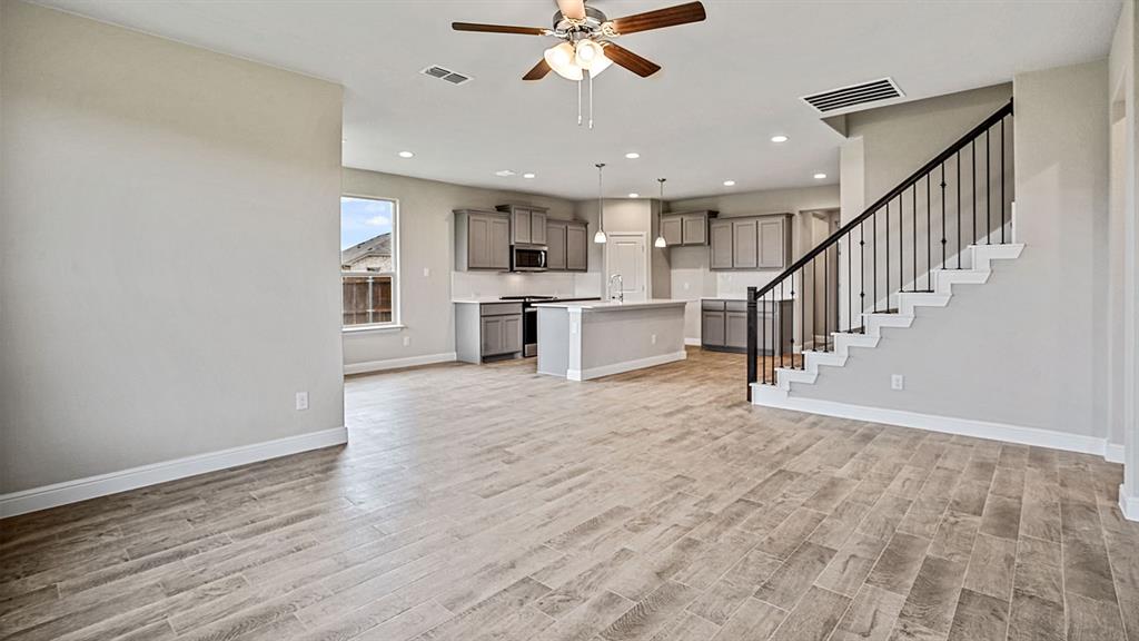 133 Hugo Court Rhome, TX 76078 - Photo 12 of 40 a view of an empty room and kitchen with window a ceiling fan and wooden floor