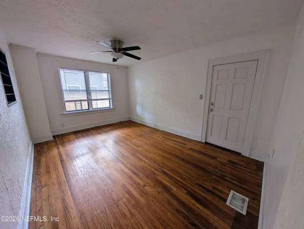 a view of an empty room with wooden floor and a window