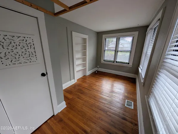 a view of an empty room with wooden floor and a window