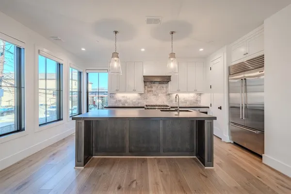 a kitchen with stainless steel appliances granite countertop a stove a refrigerator a sink and white cabinets with wooden floor