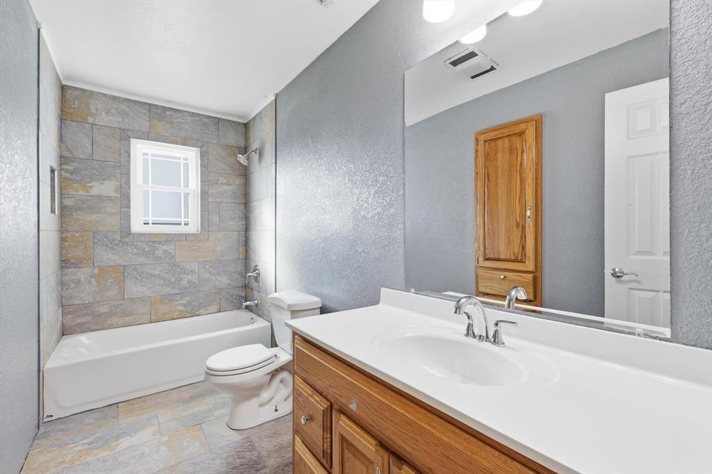 123 Valley Ranch Road Sherman, TX 75092 - Photo 20 of 40 Full bathroom featuring a textured wall, vanity, stone tile flooring, and tub / shower combination